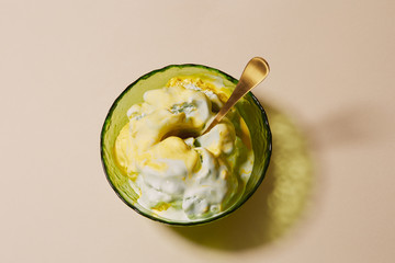 Melted ice cream with mango and mint flavor in a bowl of green glass on a light beige background. Close-up, top view.