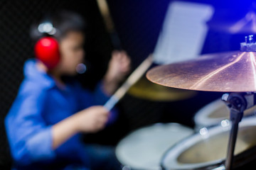 Selective focus to cymbals of drum set with blurry kid put headphone to learning and play drum set in music room. The concept of musical instrument.