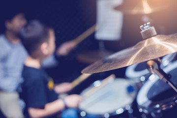 Selective focus to cymbals of drum set with blurry kid learning and play drum set with teacher in music room. The concept of musical instrument.