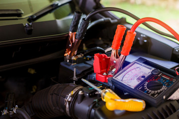 Multimeter for check voltage in battery with blurry yellow screw driver for repair service. Auto mechanic working in garage. Repair service. Selective focus.