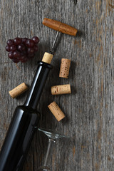 Fototapeta na wymiar Wine bottle on rustic wood tabnle with the cork pulled partially out, with grapes and corks