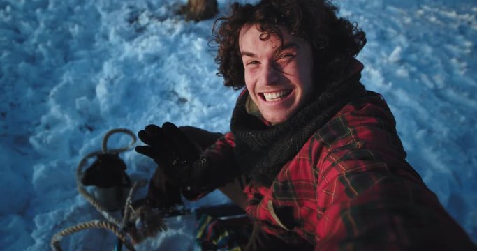 Closeup portrait of a curly hair guy tourist on the sleigh in a winter time make a funny video very excited enjoying the moment while traveling alone