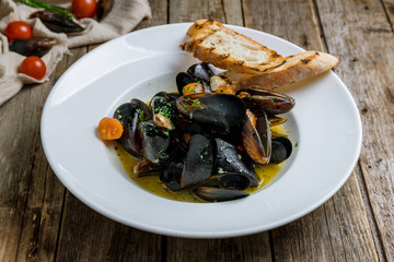 Mussels in wine sauce on white plate with tomatoes
