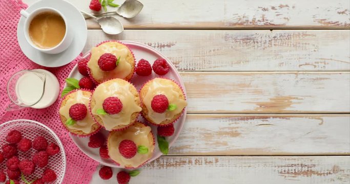 Cupcakes with white chocolate and fresh raspberries on a on a rotating ceramic plate on a wooden white table, close up. A delicious dessert or breakfast.