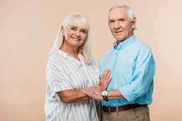cheerful senior couple smiling while standing on beige