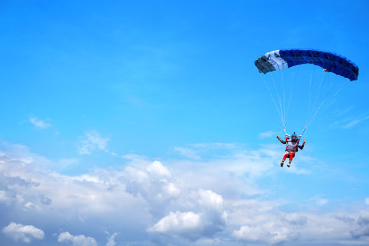 Skydiver with a dark blue canopy on the background a blue sky above clouds, close-up