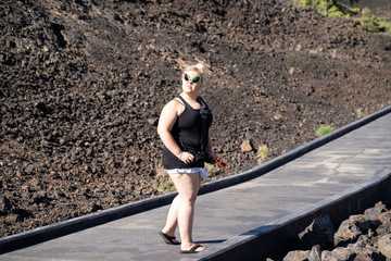 Blonde woman wearing alien sunglasses walks on a boardwalk in Craters of the Moon National Monument in Idaho. Concept for extraterrestrial - obrazy, fototapety, plakaty