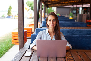 Young sensitive woman using laptop computer in the street cafe outdoor. Freelance work concept....