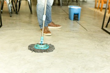 Man worker with mop and bucket cleaning floor in the cafe.