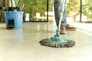 Man worker with mop and bucket cleaning floor in the cafe.