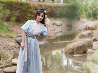 Beautiful Asian woman in cyan Chinese costume clothes hanfu standing beside of stream and listening with hand near ears gesture, traditional ancient Chinese beauty.