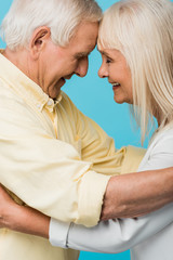 side view of happy retired couple with closed eyes smiling isolated on blue