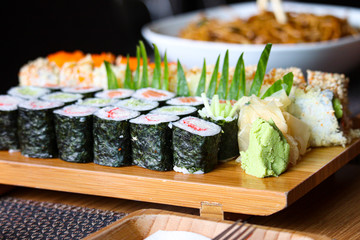 Asian food sushi rolls, wasabi and noodle on wooden plate.
