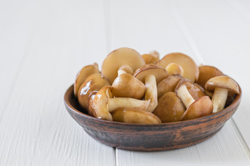 Clay bowl filled with mushrooms on the village white table.