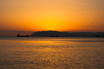 Sunset in Black sea, photographed in Crimea. Several boats sailing on horizon. Water surface rippling. Setting sun kindle clear sky. Evening seascape. Selective soft focus. Blurred background