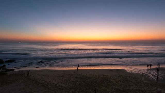 Zooming in timelapse of orange sunset above the ocean. Getting dark at Dreamland beach at Bali, Indonesia. Tourists enjoy the fresh evening, swim and take photos