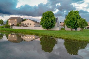 Homes and trees reflected on the shiny water of a pond amid a grassy terrain
