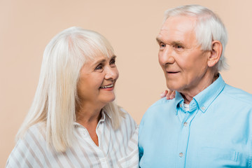 happy retired woman looking at man with grey hair isolated on beige