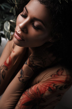 Glamour portrait of a metis young woman with perfect smooth glowing mulatto skin, full lips and fresh makeup on her face. Sensual and seductive african american female model is posing in the foliage
