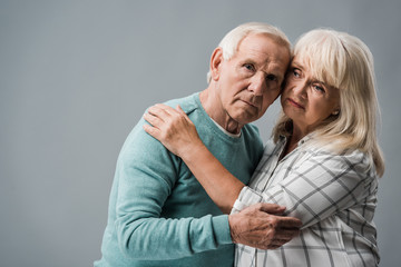senior woman with grey hair hugging upset husband on grey