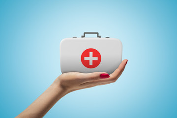 Side closeup of woman's hand facing up and holding small medical bag on light blue gradient...