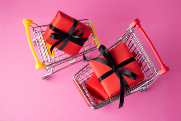 Red gift box in shopping cart on pink background