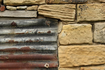 A rusty corrugated metal sheet against a stone building