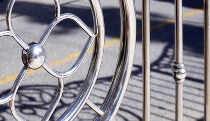 Side view of circle and floral pattern of stainless steel fence with sunlight and shadow on street surface, exterior architecture concept