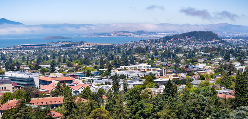 View towards Berkeley, Richmond and the San Francisco bay area shoreline on a sunny day; University of California Berkeley campus buildings in the foreground, California