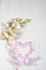 Fototapeta na wymiar Flat lay flower and stone composition consists plastic orchid, silk ribbons and 14 rose quartz hearts which are laid out in the shape of a big heart. Top view, copy space.