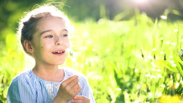 Beautiful little girl at sunny summer day blowing dandelion on green meadow. Summer fun concept.