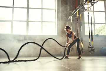 Foto op Canvas Strong and beautiful. Young athletic woman with perfect body doing crossfit exercises with a rope in the gym. © Friends Stock