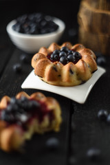 Homemade sweets. Delicious cakes with jam and raw wild bilberries on oak cutting board selective focus copy space. Low key still life with natural lighting