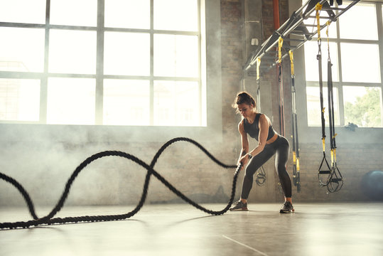 Strong and beautiful. Young athletic woman with perfect body doing crossfit exercises with a rope in the gym.