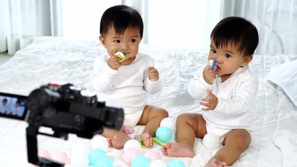 two twin babies on a bed with video camera recording - Powered by Adobe