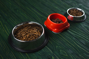 bowls with pet food in row on green wooden surface