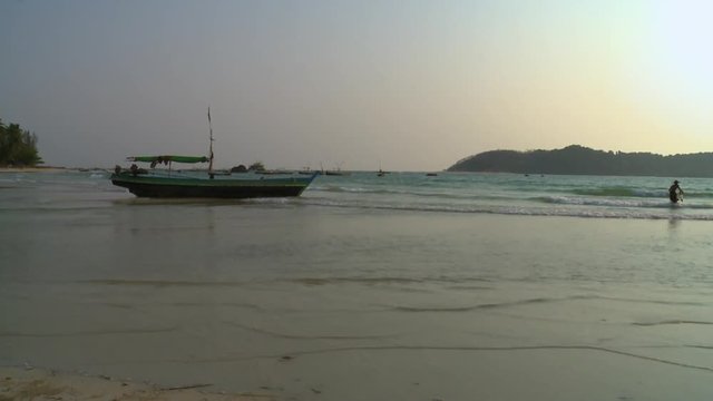 Wide low-angle evening still shot of a stationary fishing boat, and silhouette of a local Burmese fisherman netting fish near the sea shore, Ngapali Beach, Myanmar