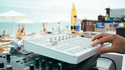 Summer beach party. DJ turns the controls on the mixing console. People are having fun on the back blurred background.