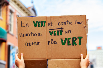 Environmentalist holds French sign. A closeup view of a French sign, saying in green and all against walks towards a greener future, held by an ecological activist during a protest in a city center.