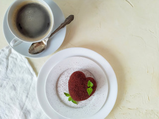 One heart shaped cake decorated with chocolate biscuit crumbs and mint on a round plate next to a Cup of coffee on a light background top view.