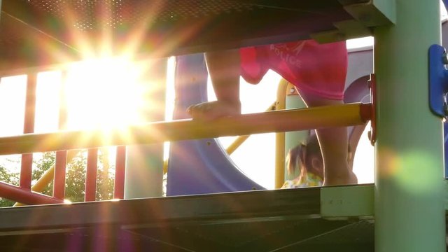 Portrait of Asian little child girl having fun while climbing on steel bar for trapeze in playground on summer day.