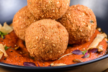 A serving of deep fried 'croquettes' in a dark colour bowl, on a red tomato sauce