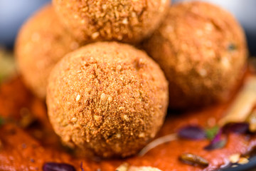 A serving of deep fried 'croquettes' in a dark colour bowl, on a red tomato sauce