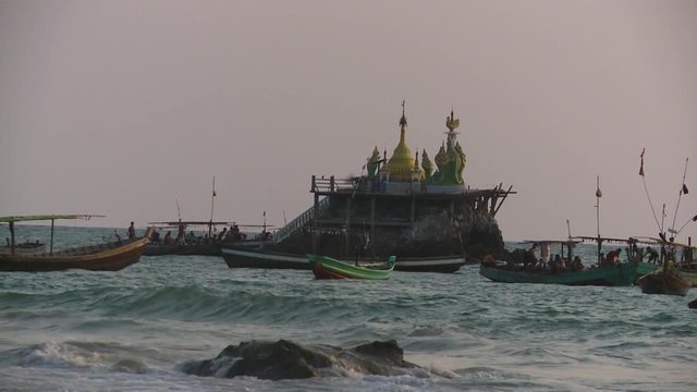 Wide low-angle still shot of Burmese fishing boats anchored a round a sea rock with a gold-painted stupa on its top, a way from Ngapali beach, Thandwe, Rakhine State, Myanmar