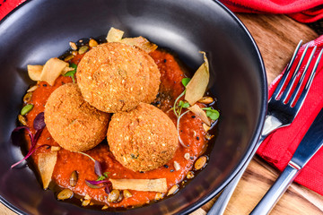 A serving of deep fried 'croquettes' in a dark colour bowl, on a red tomato sauce