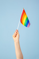 Closeup of a hand waving a small rainbow flag against a light blue background