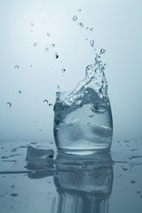 High splash with splashes of pure cold water. Ice falls into a glass
