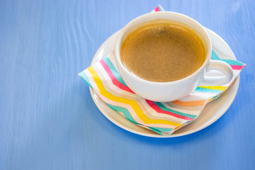 A cup of coffee with froth, white porcelain ceramics, color striped napkin.