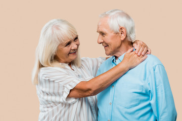 happy retired woman hugging senior husband isolated on beige