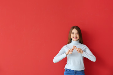 Young deaf mute woman using sign language on color background © Pixel-Shot